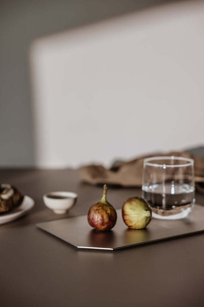 Dekotablett mit frischen Feigen und einem Glas Wasser auf einem Tisch, elegantes Design in mattem Edelstahl.