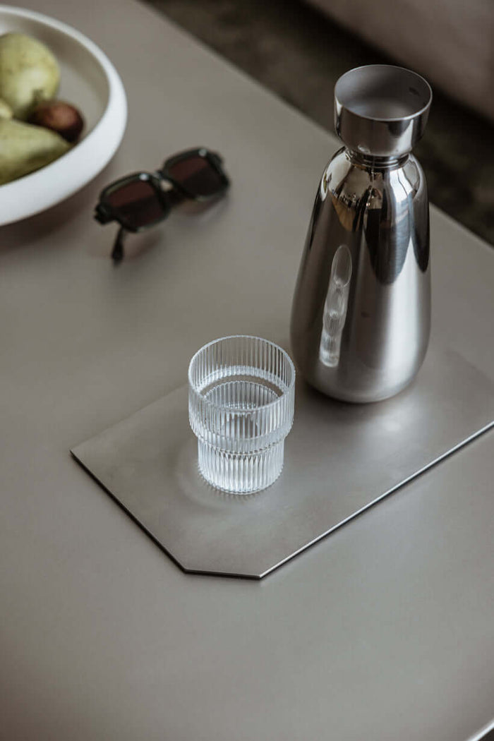 Dekotablett aus Edelstahl mit Glaskrug und Glas auf einem Tisch, modernes und elegantes Design.