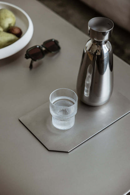 Dekotablett aus Edelstahl mit Glaskrug und Glas auf einem Tisch, modernes und elegantes Design.