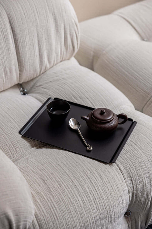 Hochwertiges Tablett aus Stahlblech mit Teekanne und Tasse auf einem hellen Sofa.