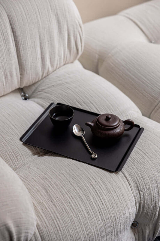 Hochwertiges Tablett aus Stahlblech mit Teekanne und Tasse auf einem hellen Sofa.