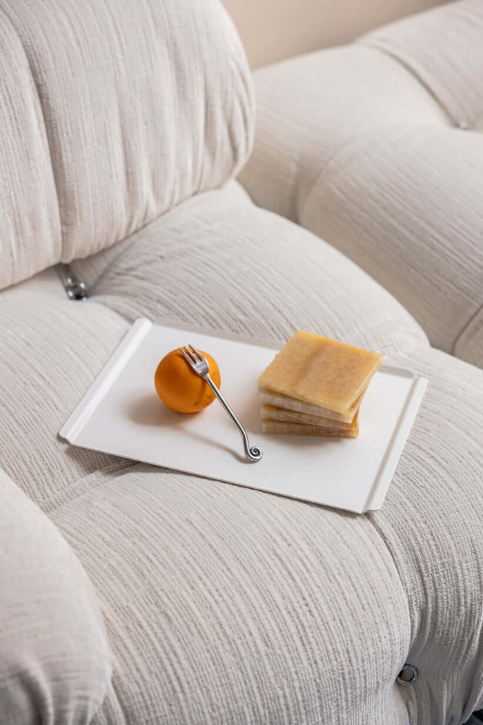 Tisch mit einem Tablett, einer Orange, einem Besteck und einigen Snacks auf einem bequemen Sofa.