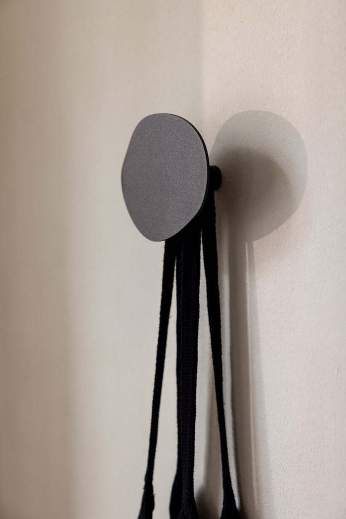 Wandhaken LOU in minimalistischem Design an der Wand mit schwarzen Bändern zum Aufhängen.